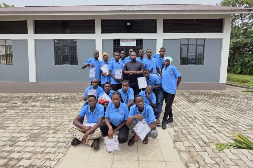 A group of students in matching blue shirts holding graduation certificates pose for a photo in front of a school building.